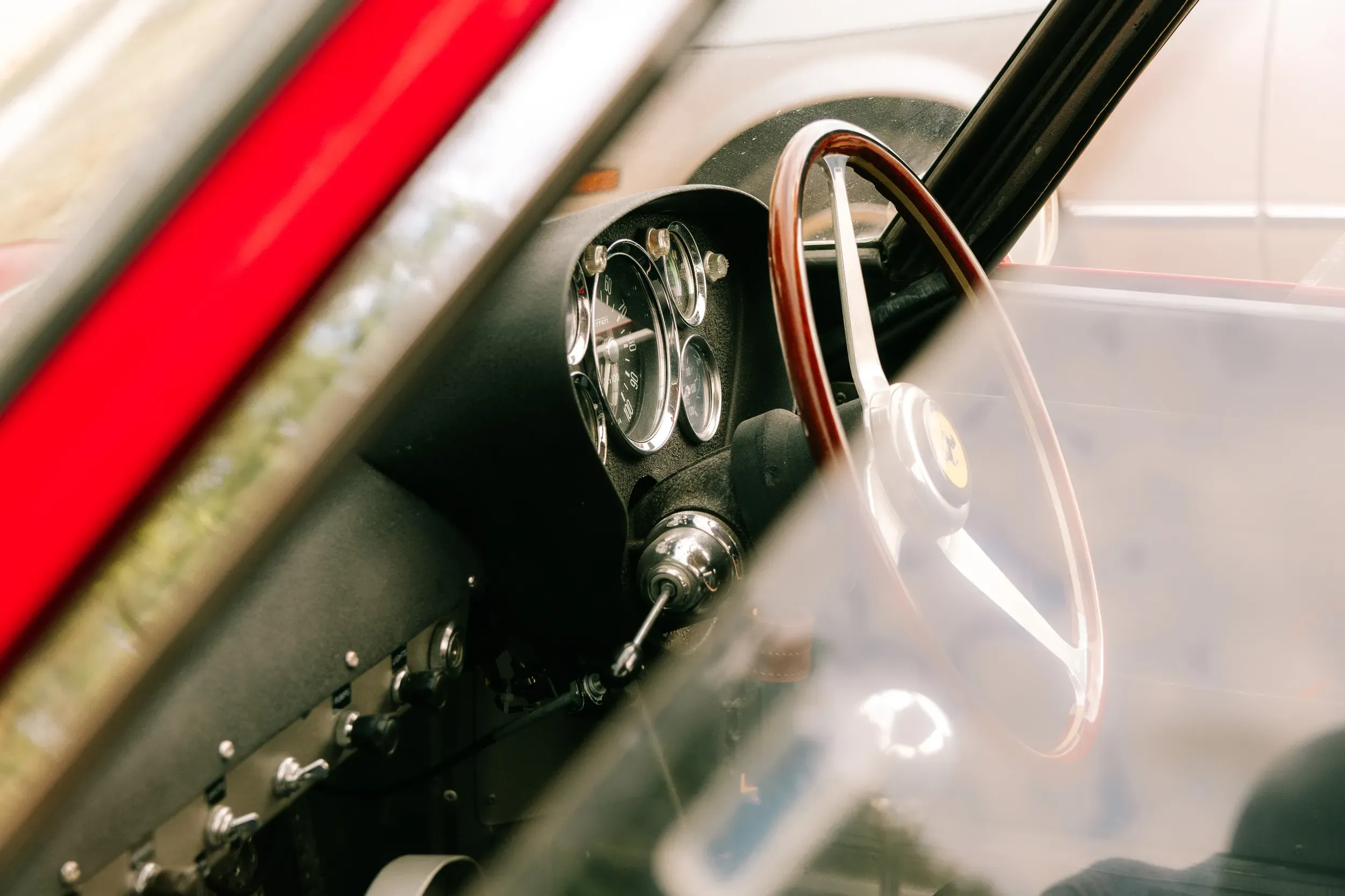 A wood-rimmed steering wheel and a cluster of dials seen through the screen of a classic Ferrari.