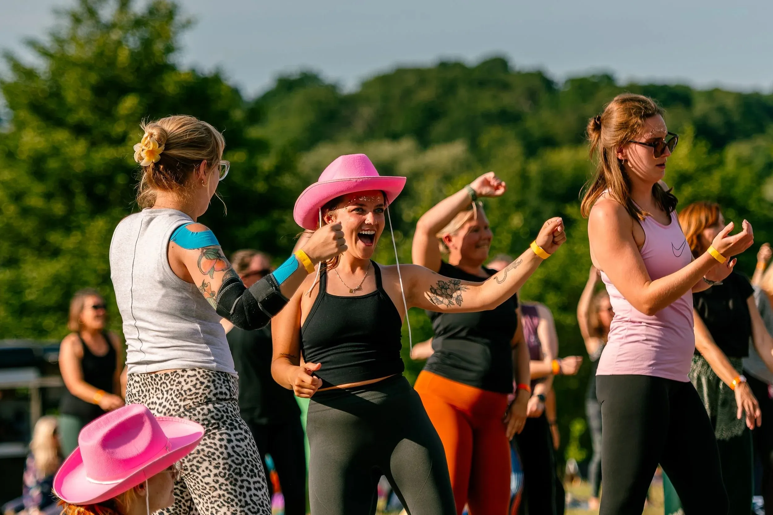 Women in pink cowboy hats laughing and dancing together outdoors.
