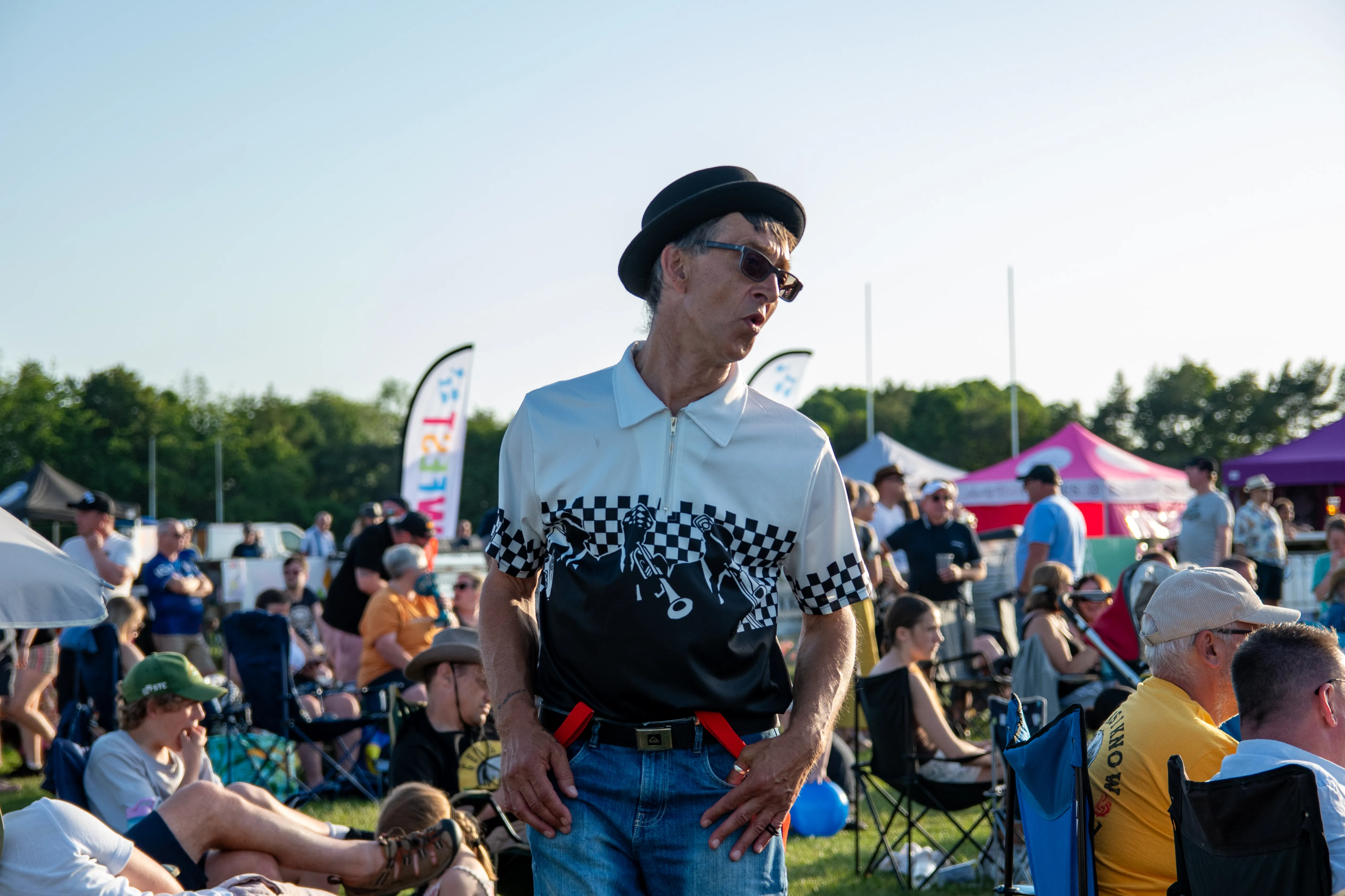 A man in a checked shirt and hat skanking in front of the crowd.