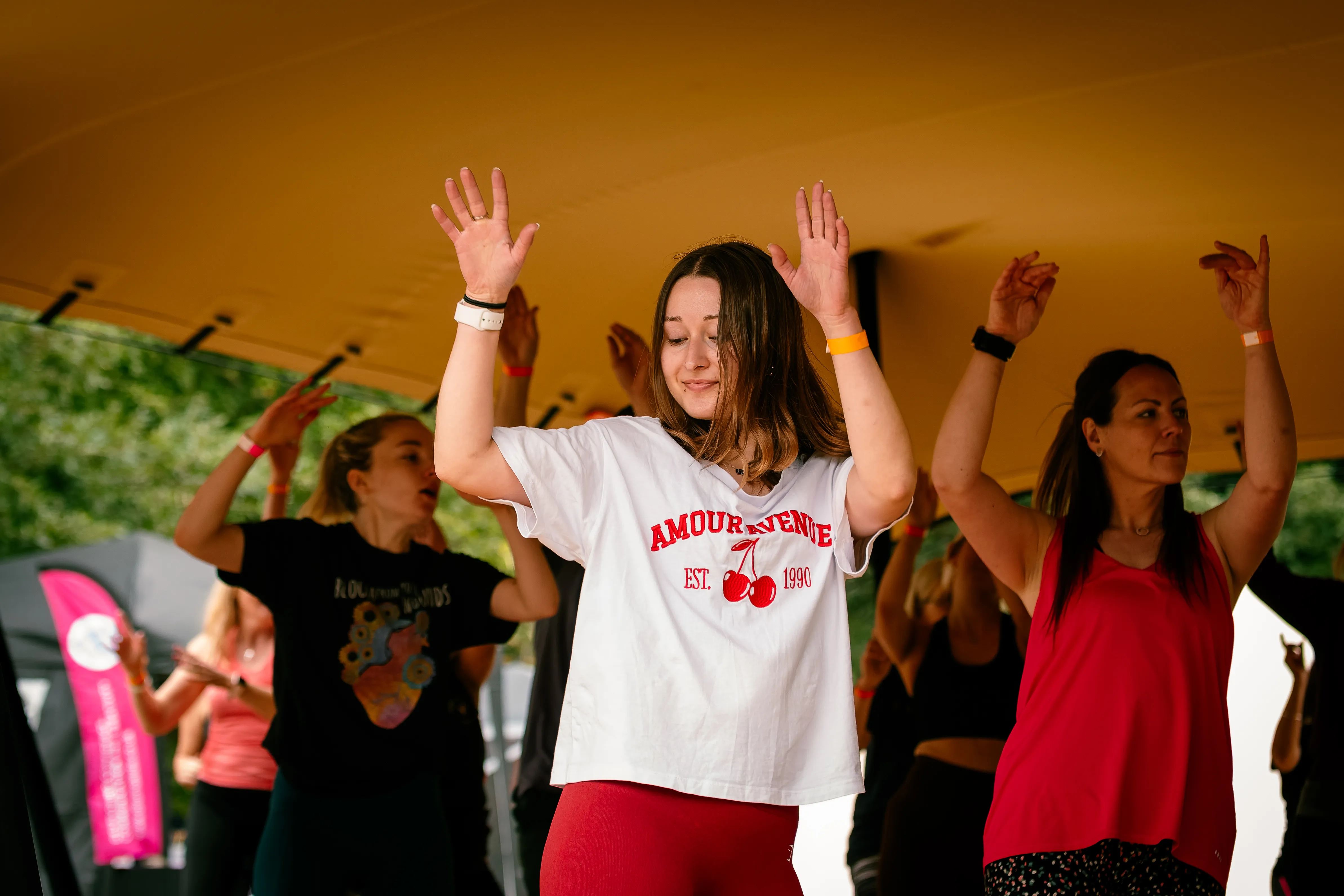A woman in a white t-shirt dancing with both arms raised during a live set.