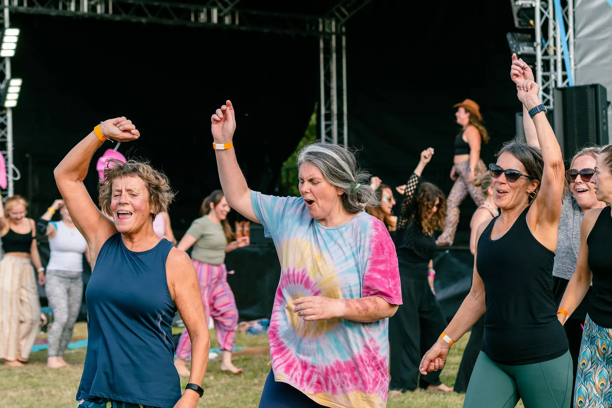 Women dancing in front of the main stage, arms up mid-song.