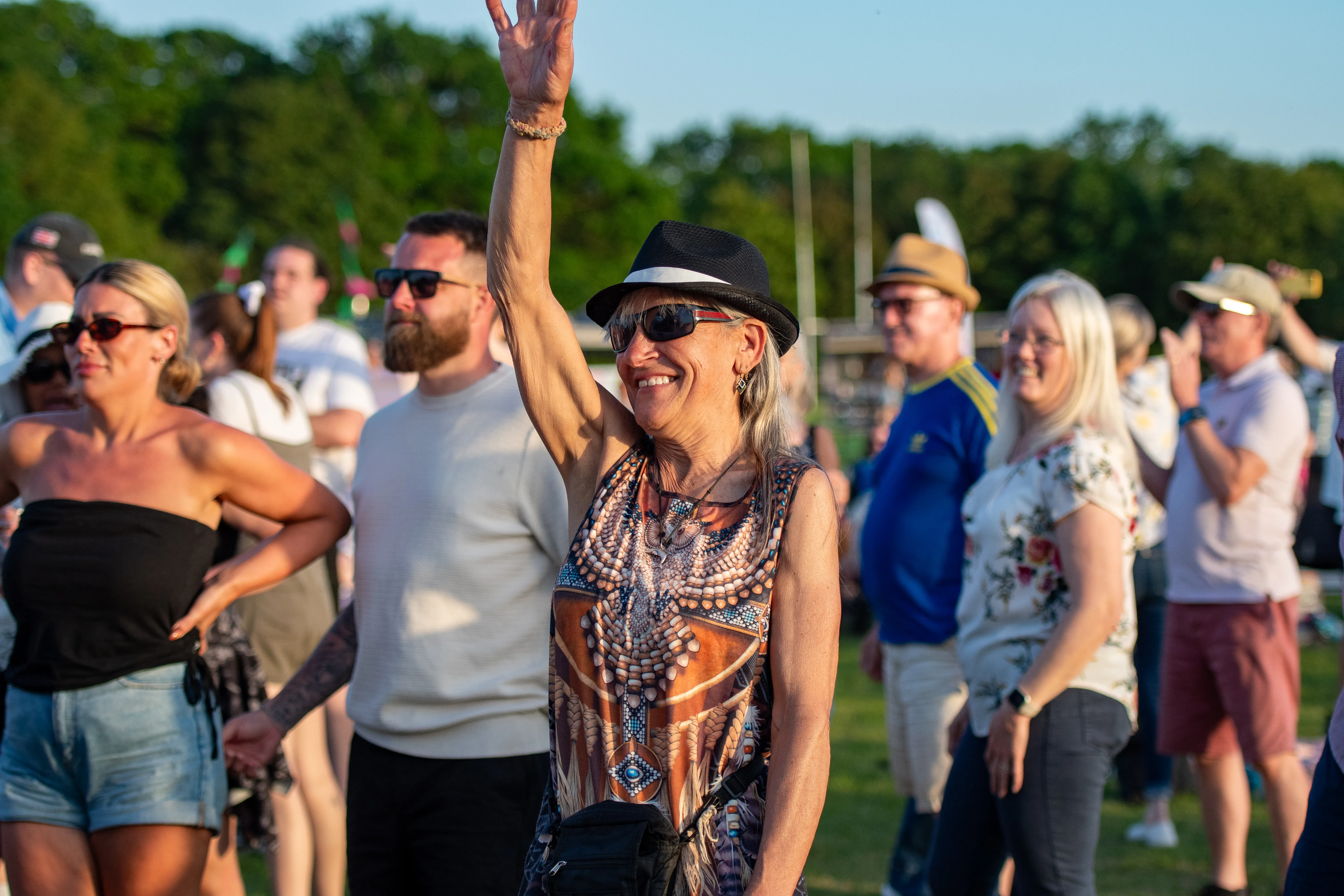 Festivalgoers waving towards the stage in the evening sun.