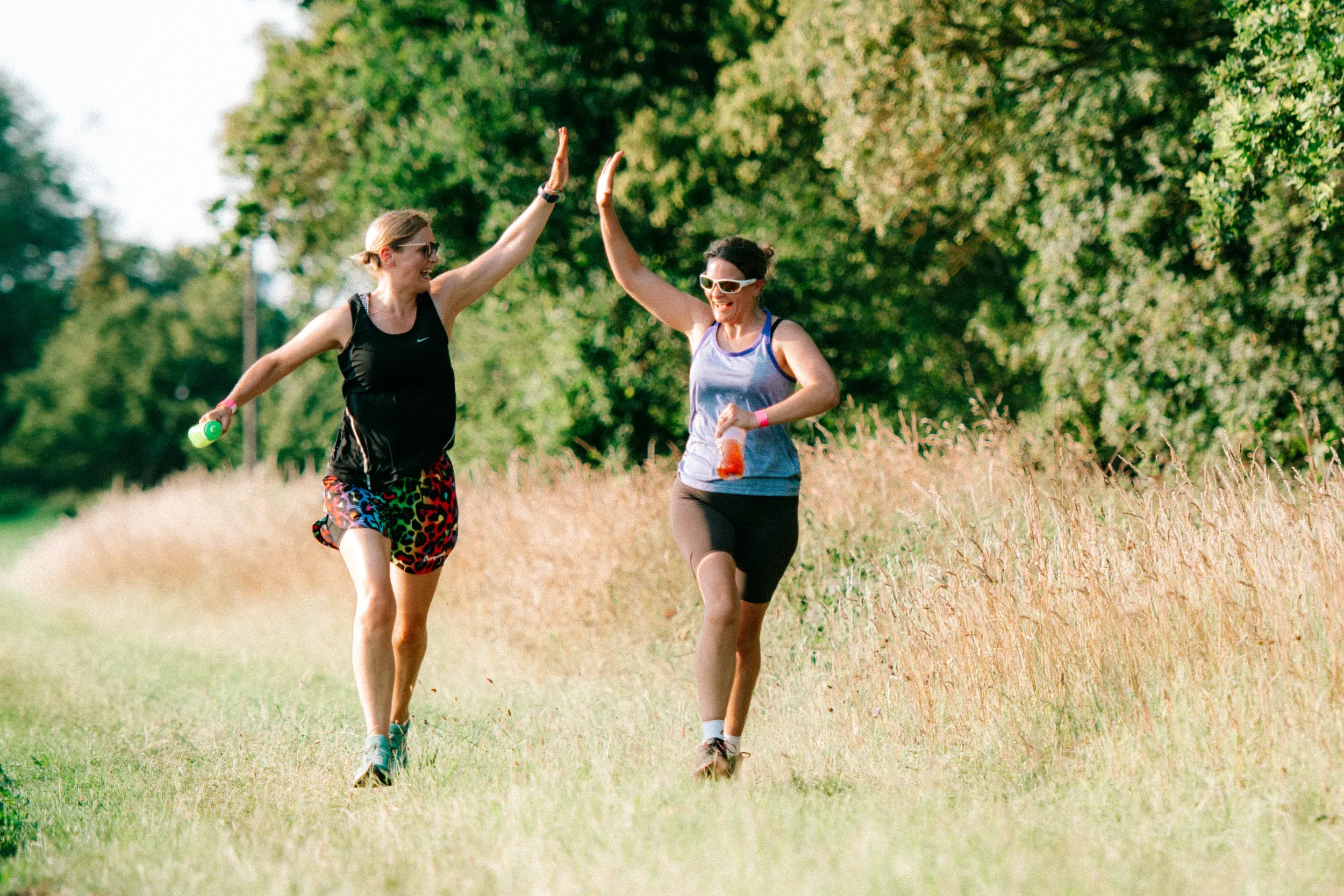 Two runners high-fiving mid-stride on a grass path, both laughing.