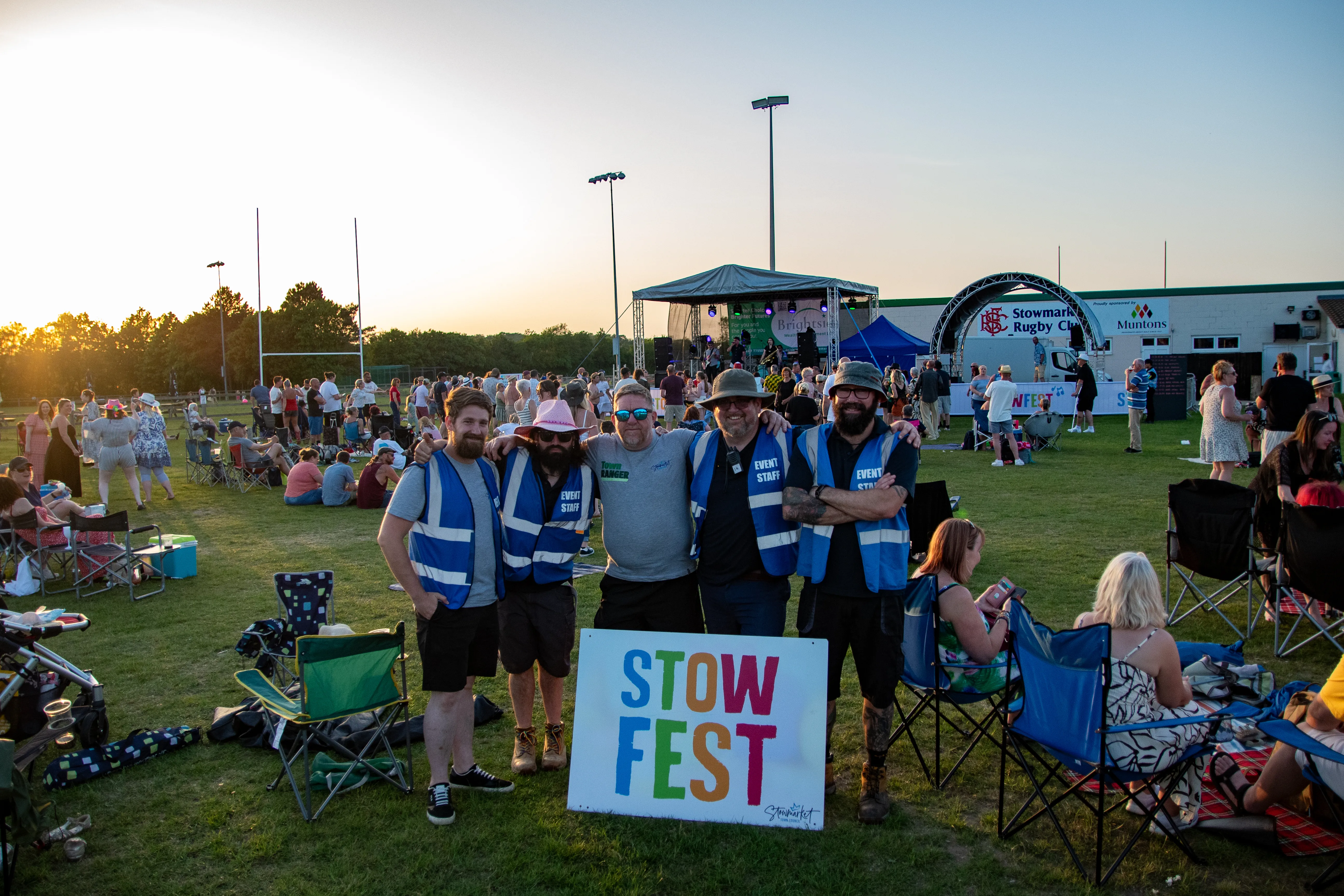 Volunteers in hi-vis holding the Stow Fest sign as the sun drops.
