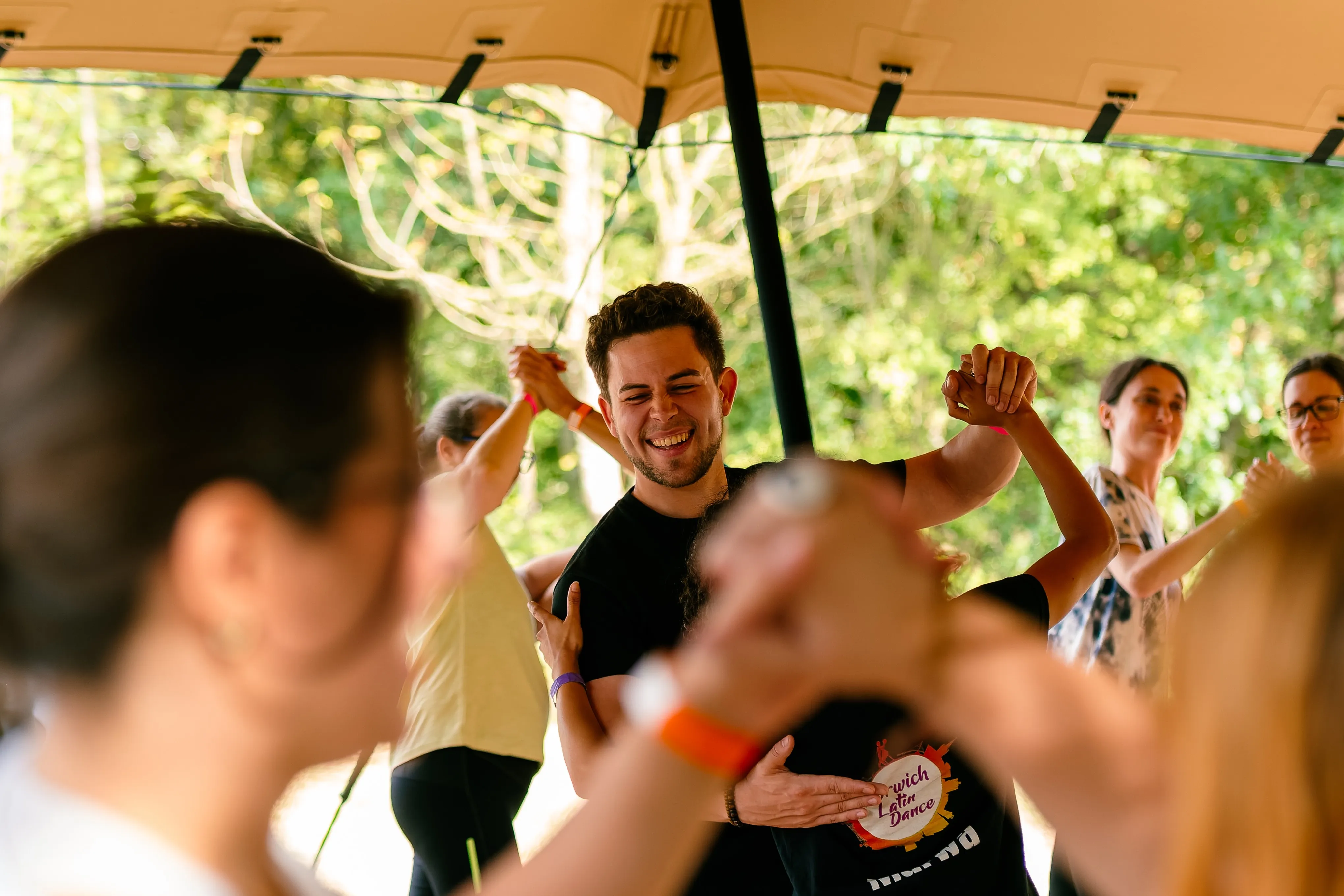 A man dancing with his arms raised under a canopy at an outdoor festival.