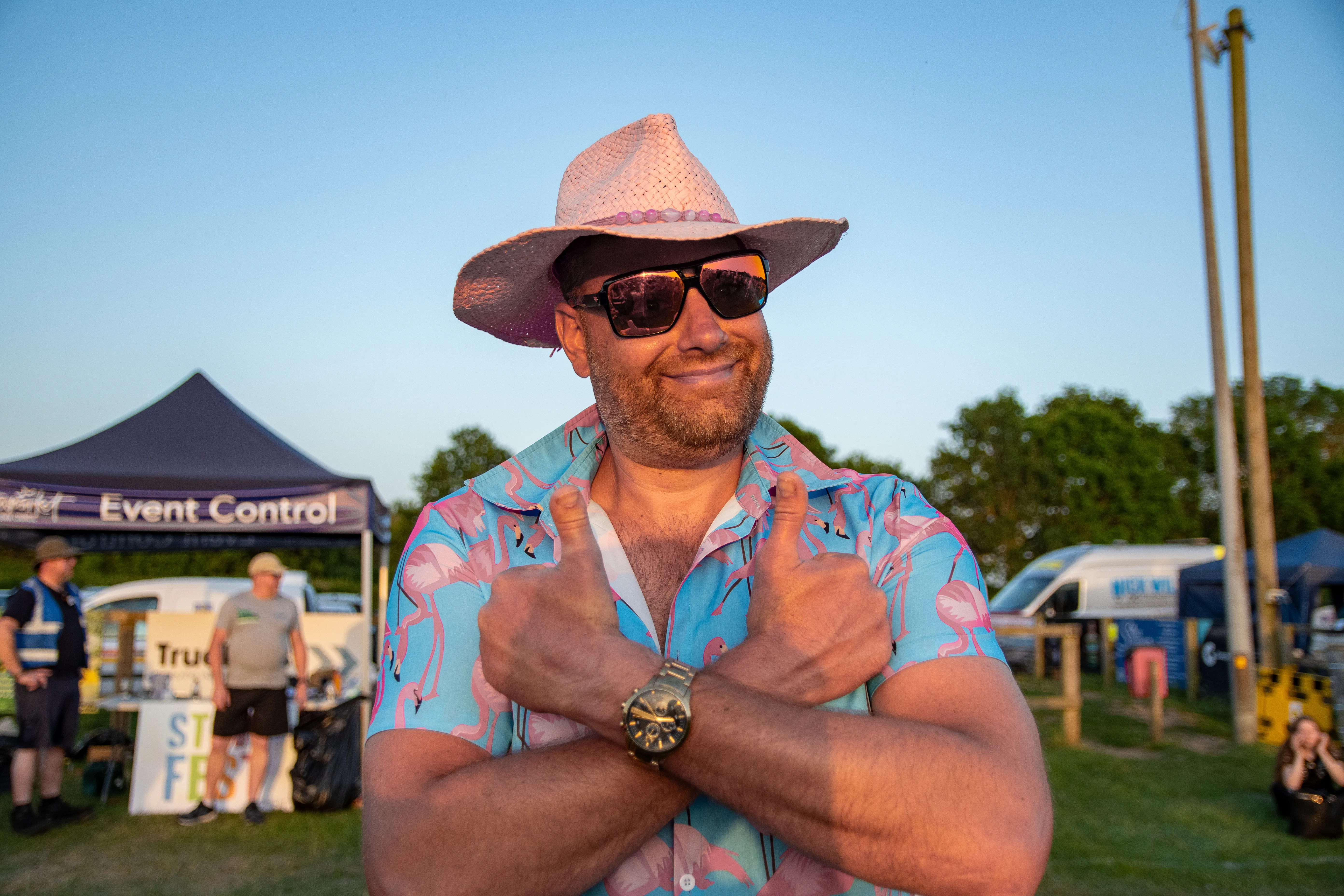 A steward in a pink hat and party shirt with arms crossed at event control.