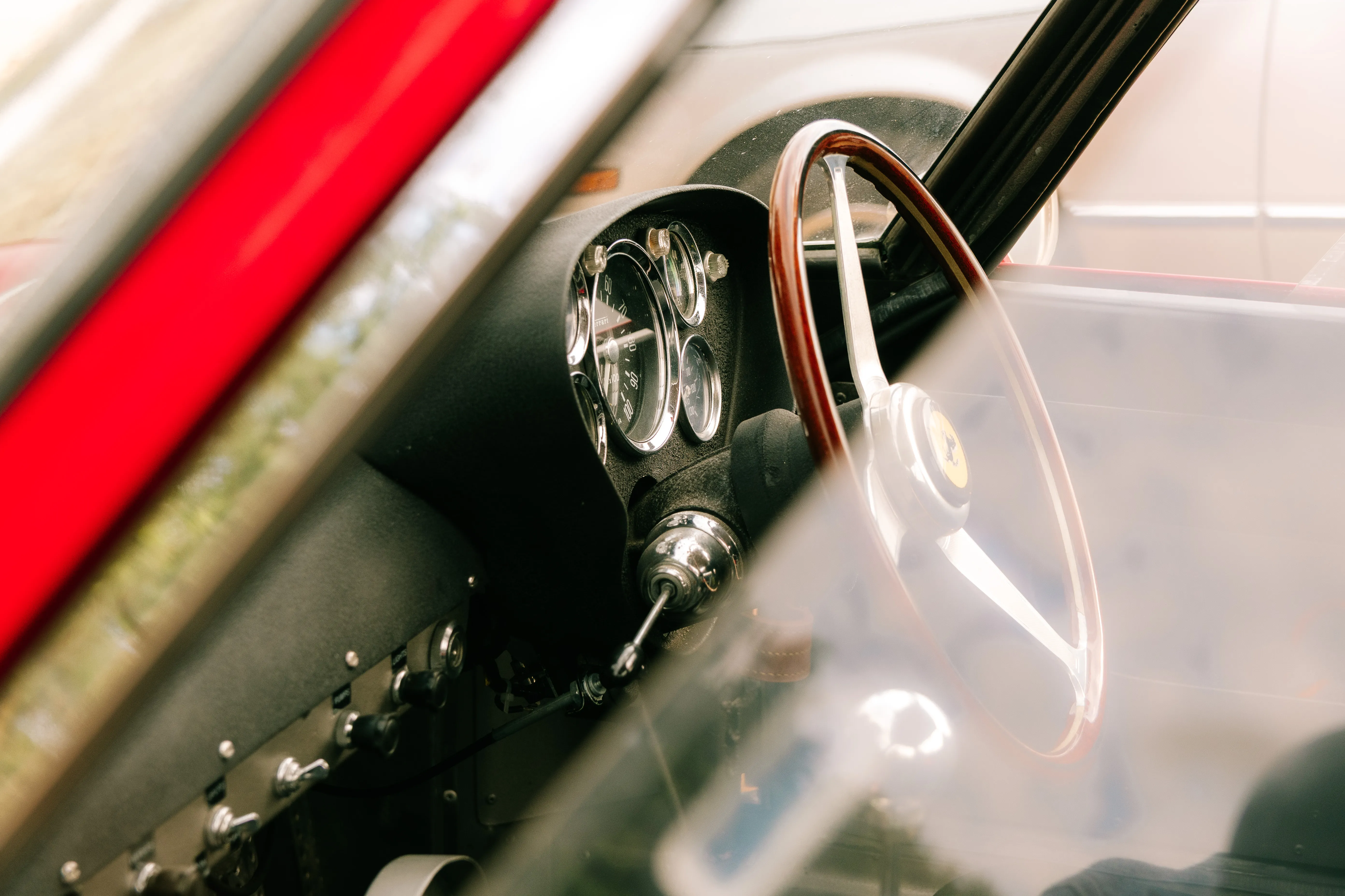 A wood-rimmed steering wheel and a cluster of dials seen through the screen of a classic Ferrari.