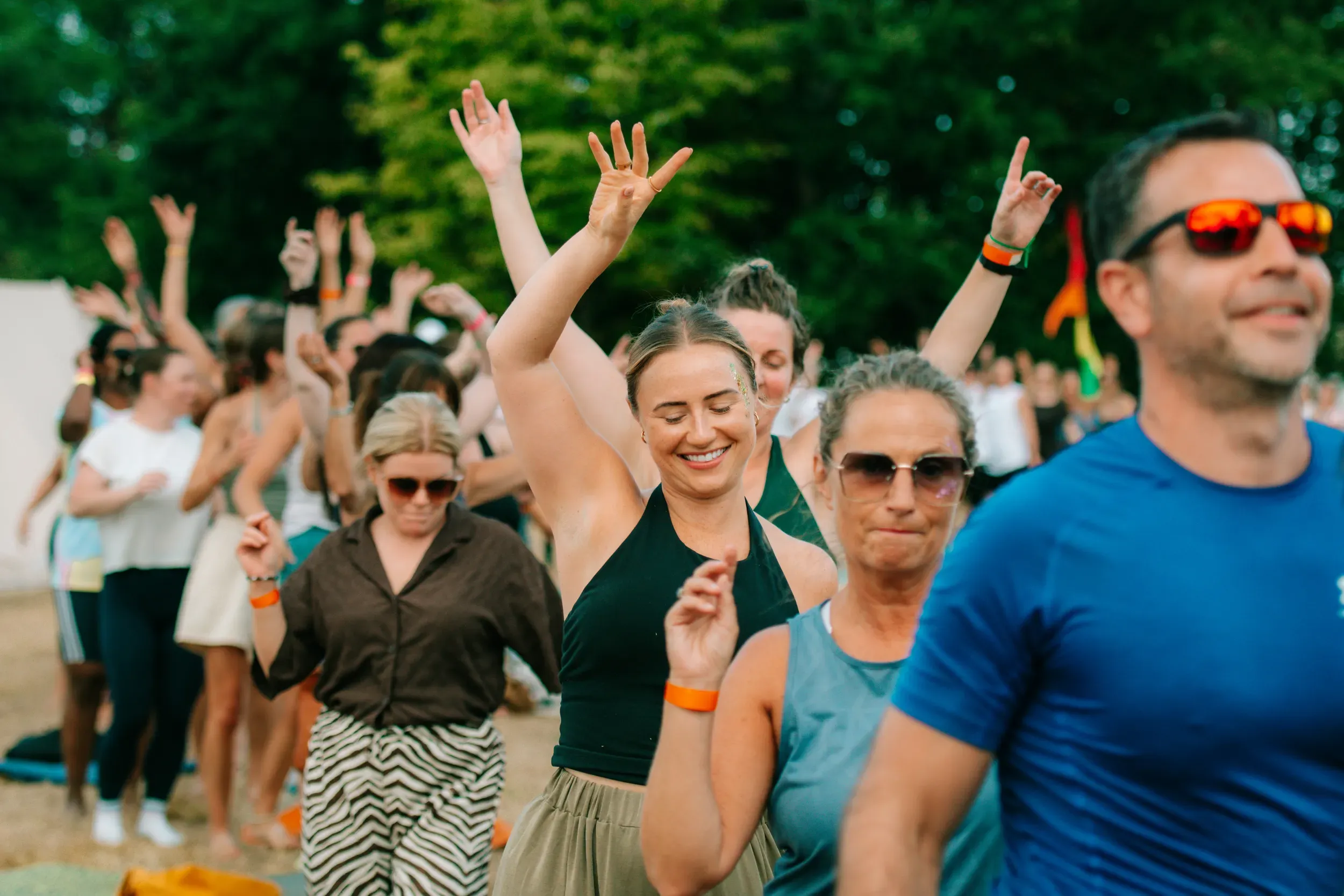 A field of people with their hands raised, following the class together in the evening light.