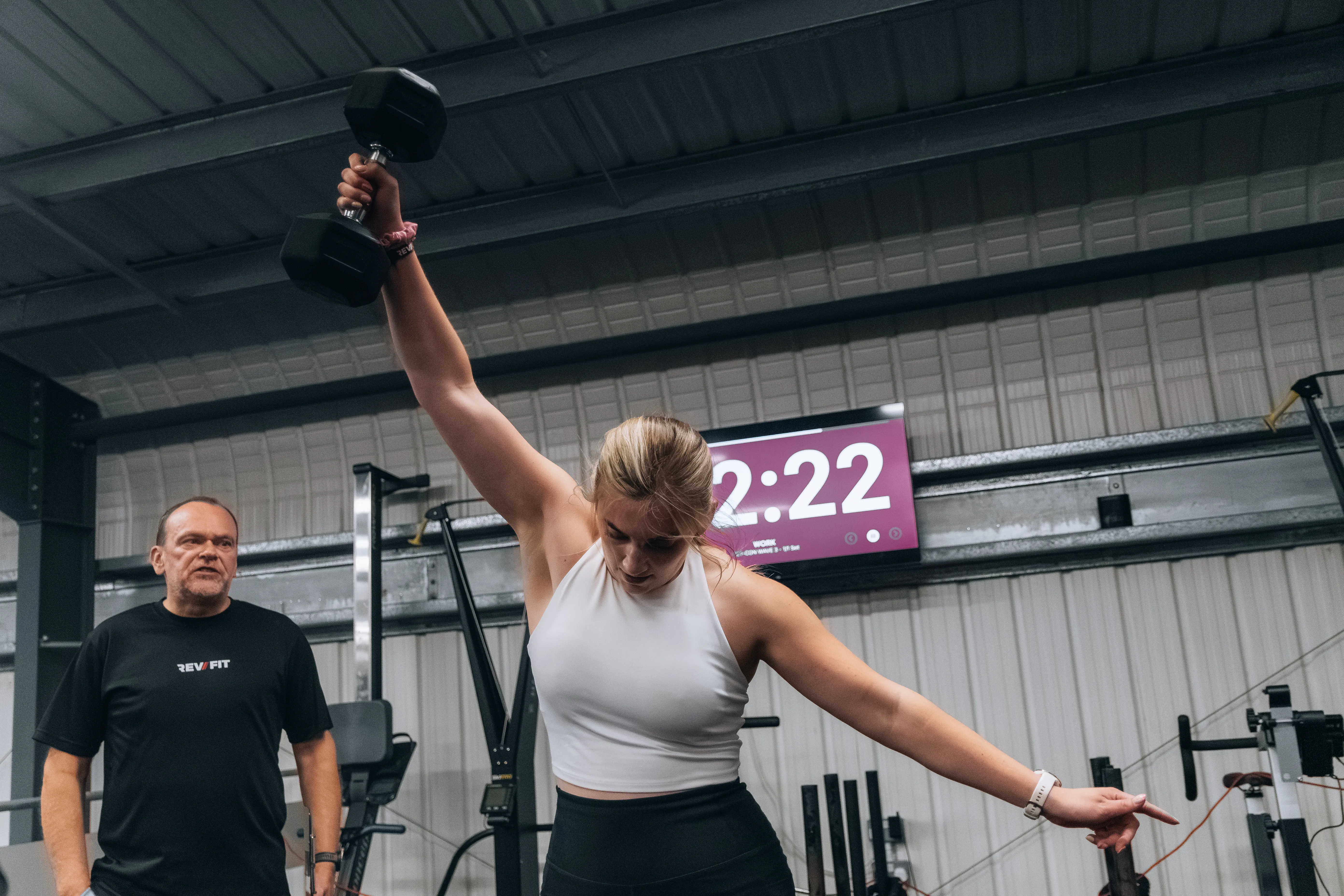 A competitor lunging with a dumbbell overhead as the clock runs.
