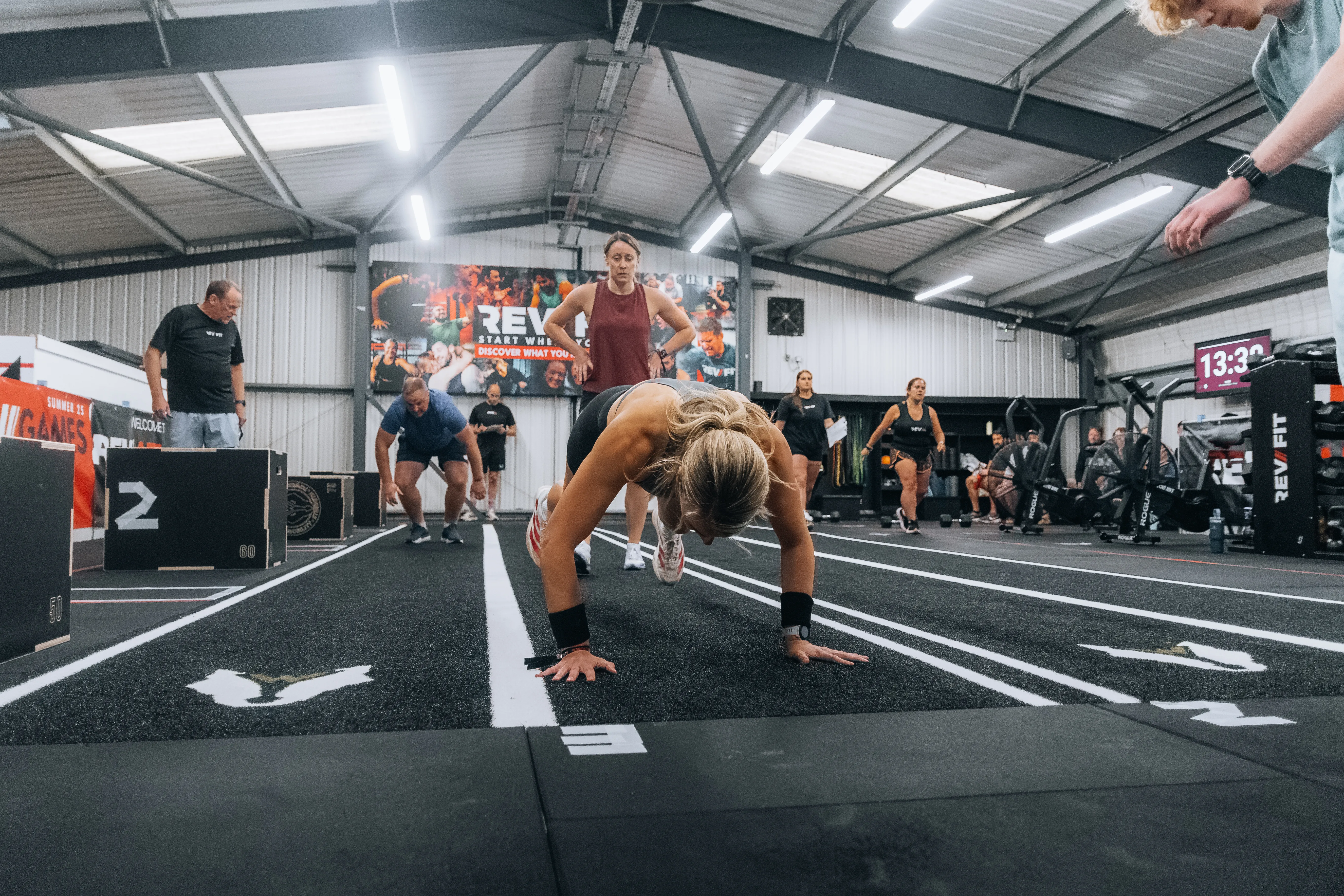 Competitors down in burpees along the gym track.