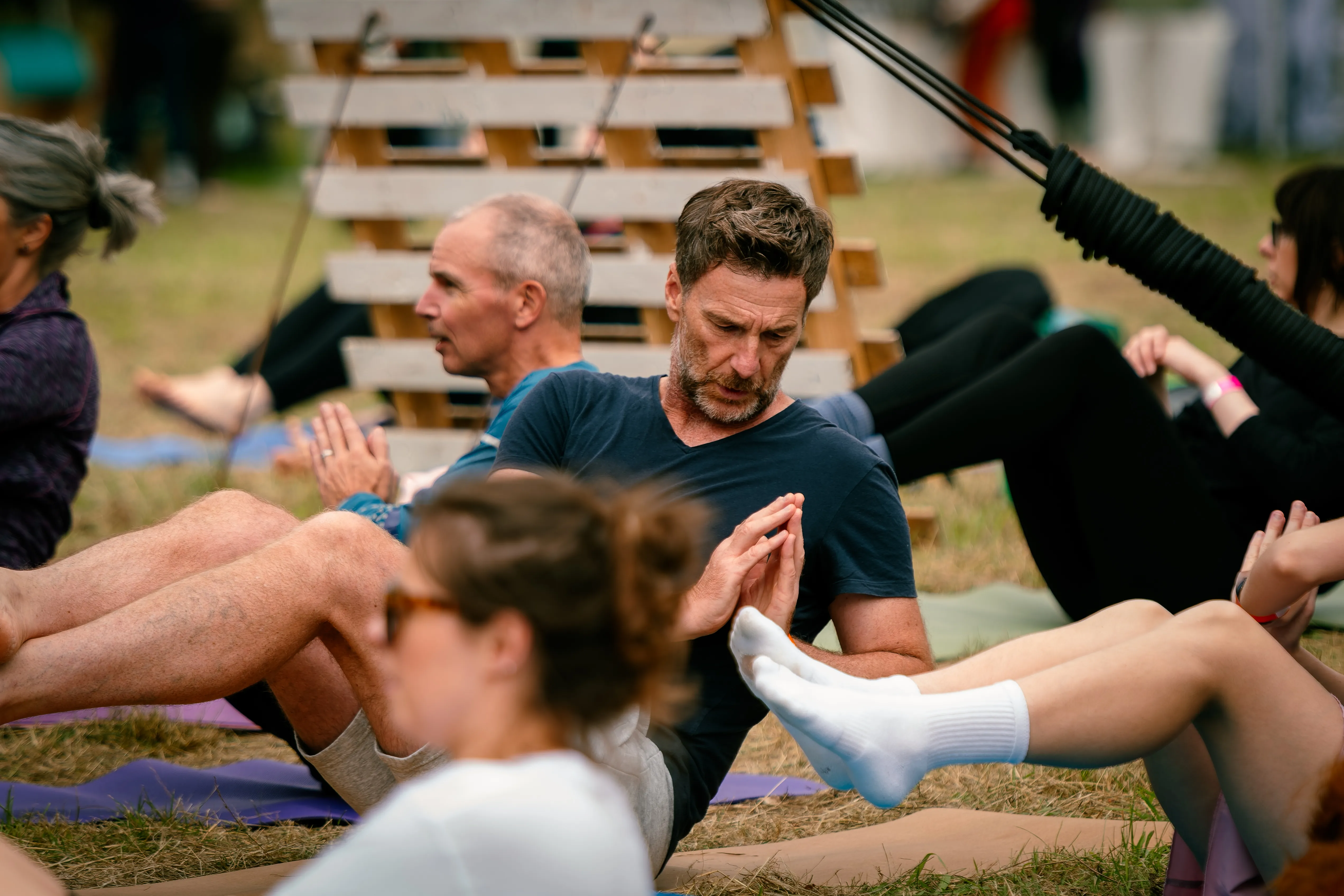 A man balancing mid-sit-up with his palms pressed together during a core class on the grass.