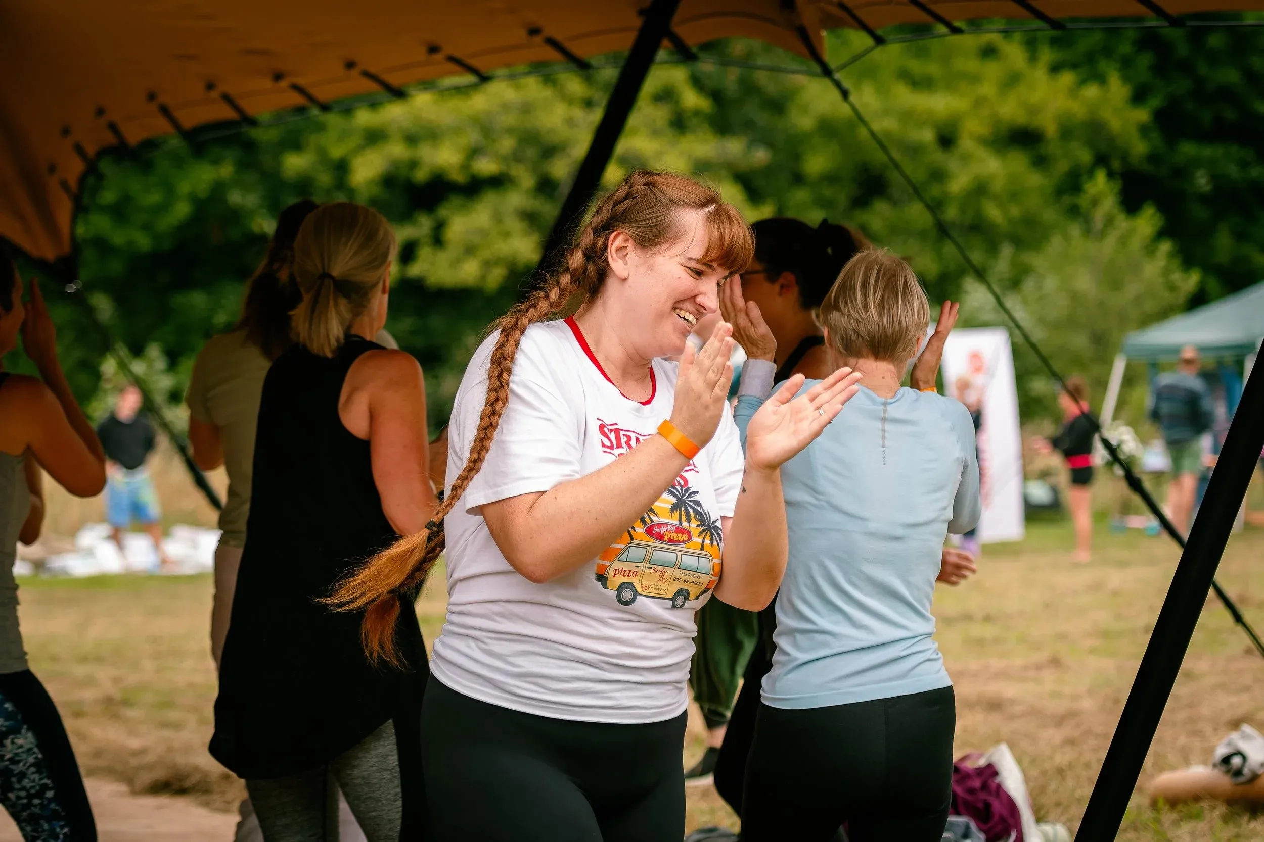 A woman in a white t-shirt clapping with her eyes closed under a canopy.