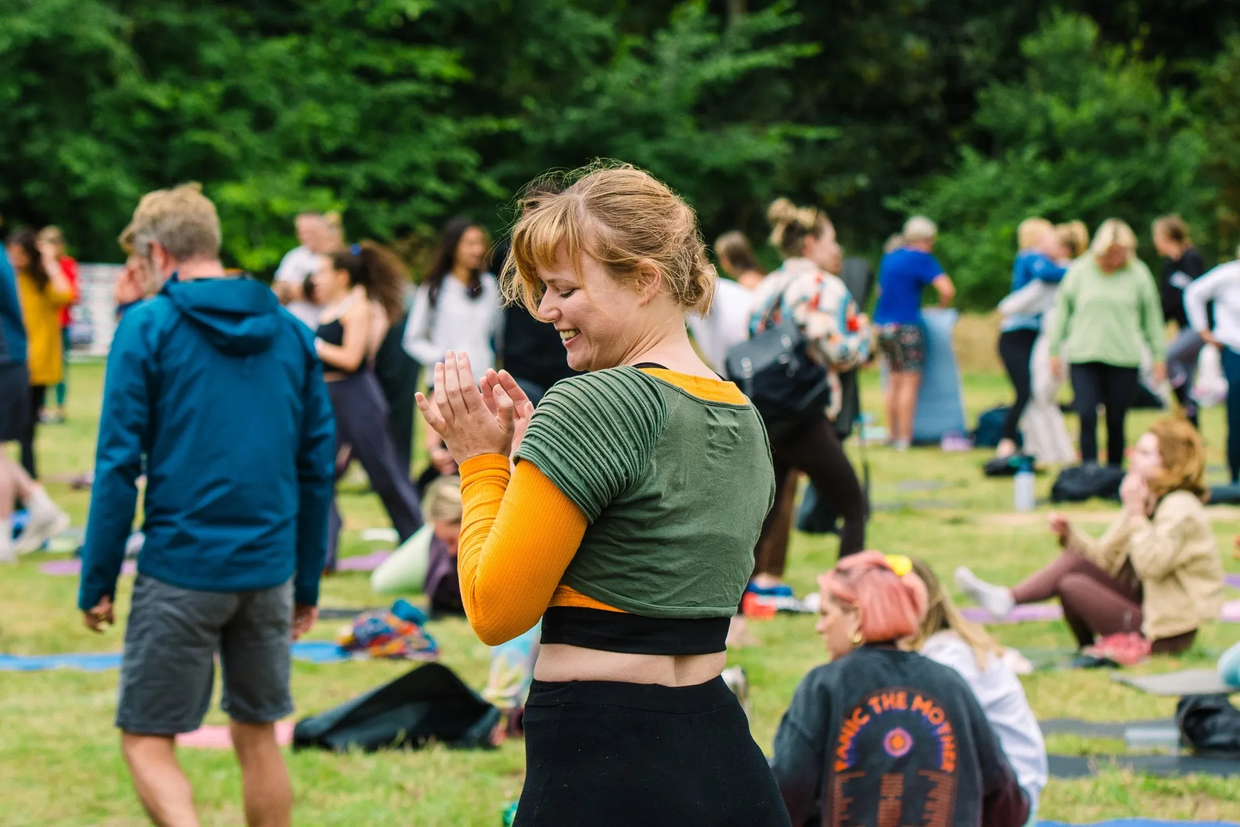 A woman in a green crop top clapping and dancing, a field of people behind her.
