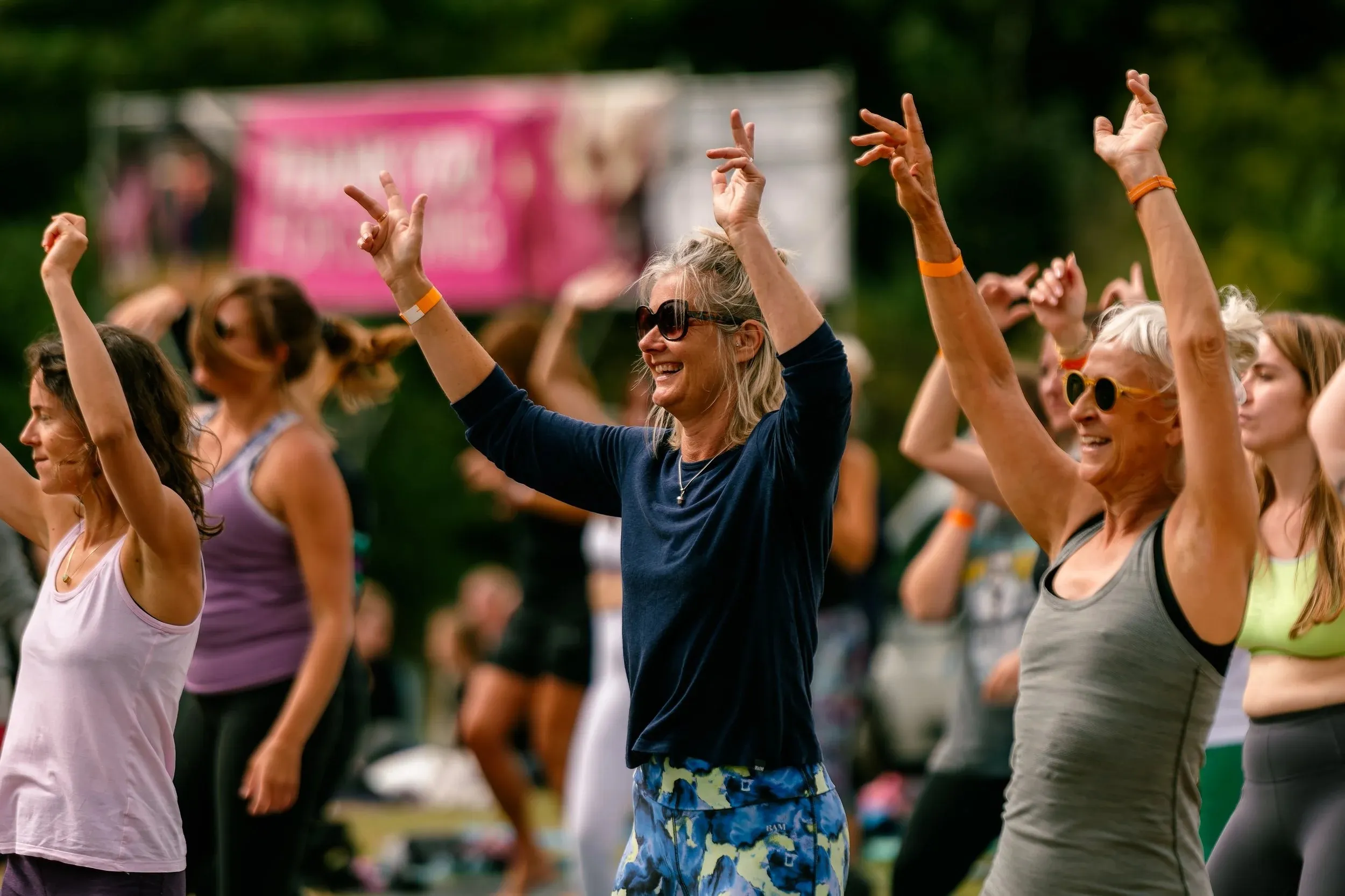 People in sunglasses with their arms raised, dancing in front of a banner.